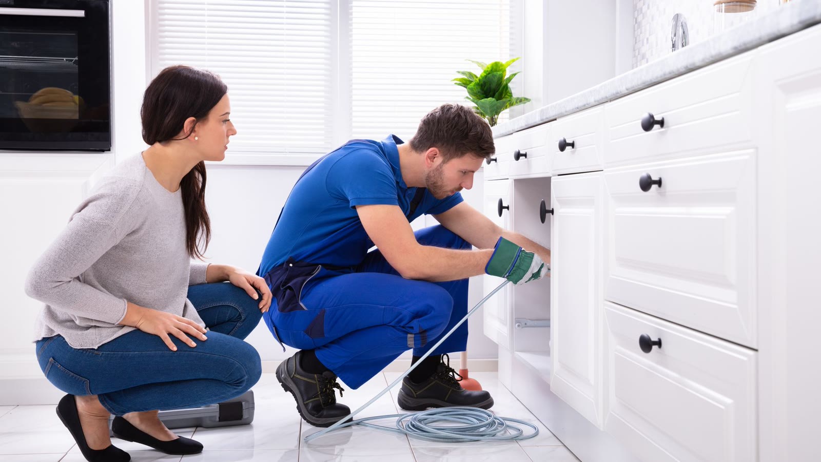 Plumber performing a drain camera inspection beneath a kitchen sink